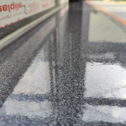 Floorwit Vitalii Mezhduhornyi - Błyszcząca, szara posadzka z widocznym odbiciem okna i fragmentem ramy okiennej z napisem 'aliplast'.