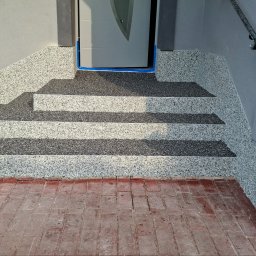 Floorwit Vitalii Mezhduhornyi - Granitowe schody wejściowe z dwukolorową powierzchnią, zabezpieczone niebieską taśmą malarską przy progu drzwi, z widoczną czerwoną kostką brukową przed nimi.