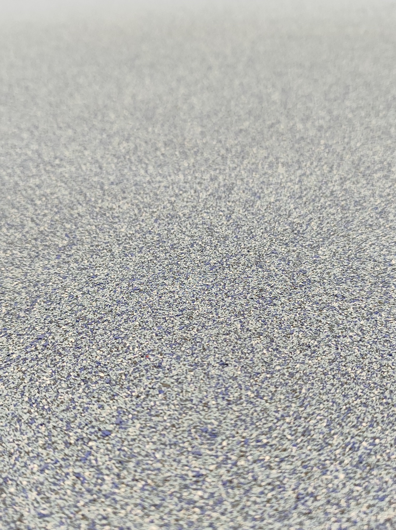 Szara posadzka z drobnymi niebieskimi i białymi plamkami, sfotografowana pod kątem, ukazująca teksturę powierzchni.