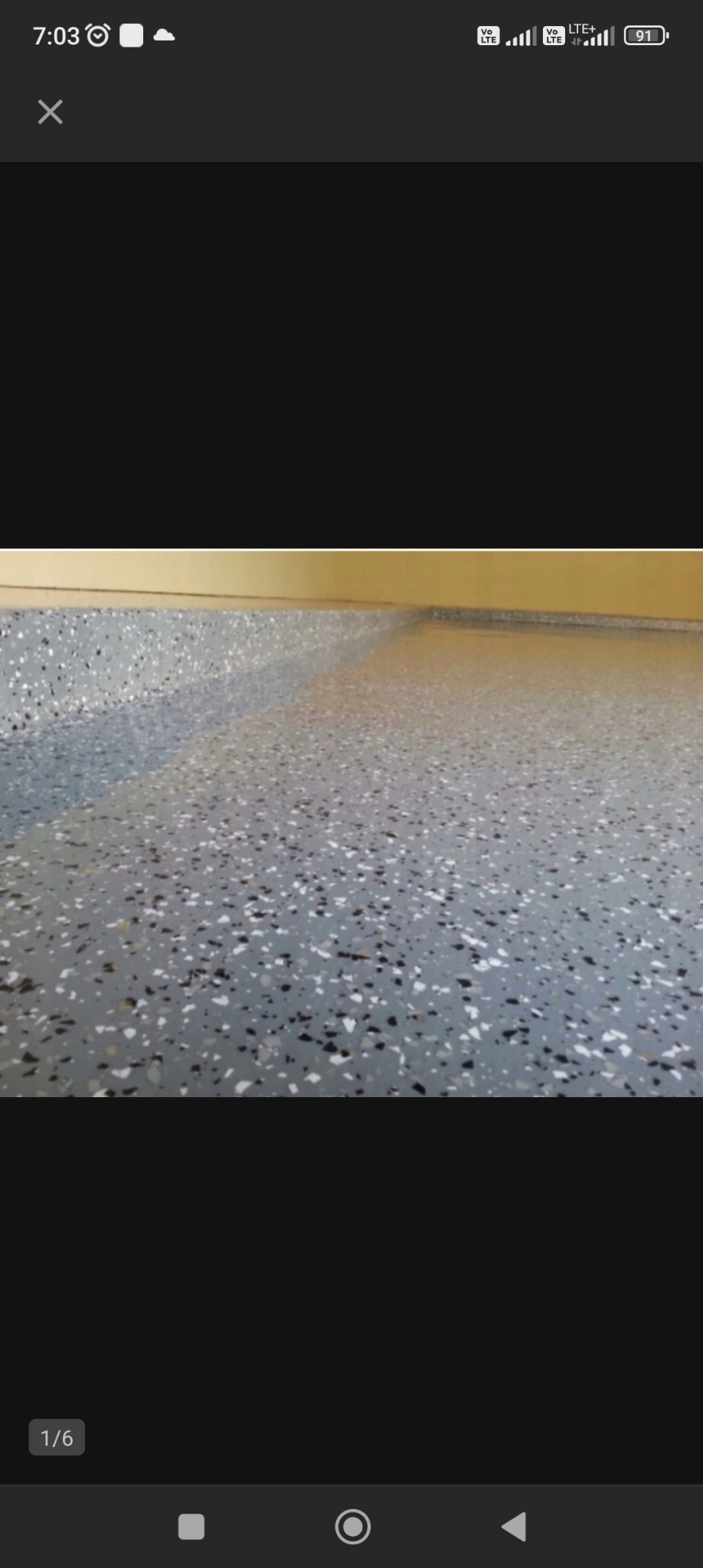 Szara, gładka podłoga z drobnymi, nieregularnymi plamkami w kolorze czarnym i białym, widoczna przy ścianie pomalowanej na jasny, ciepły odcień żółci.