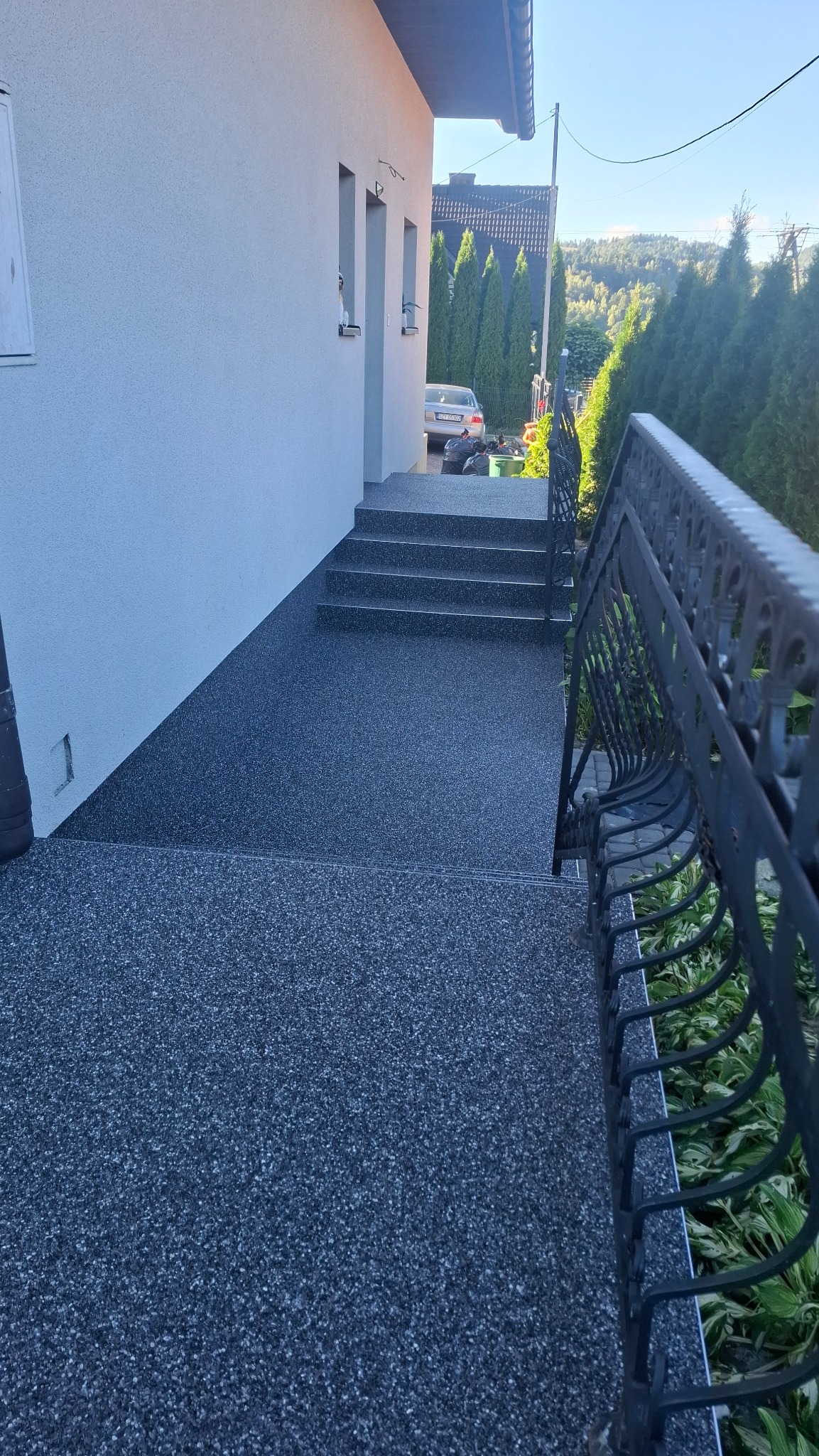 Wykończone schody i taras z szarej, drobnoziarnistej nawierzchni w Bielsko-Białej. Metalowa balustrada i jasna elewacja budynku w tle. Widok z góry.