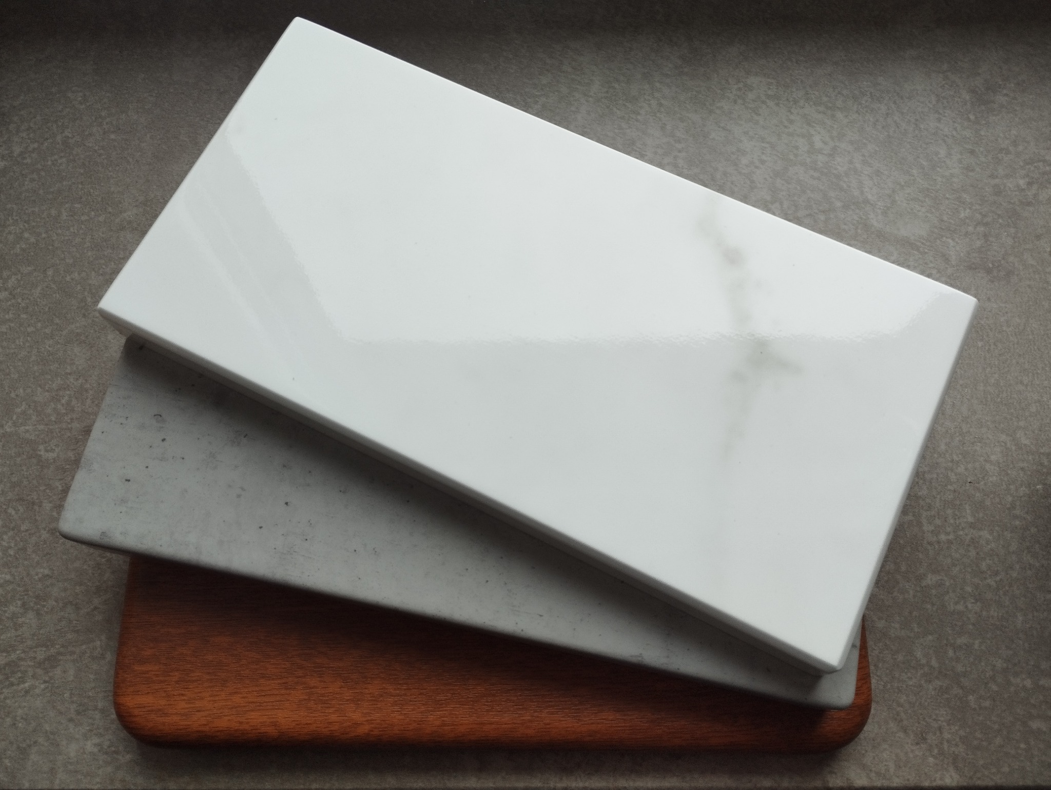 Próbki parapetów w Gliwicach: biały imitujący marmur, szary imitujący beton i drewniany, ułożone warstwowo na szarym tle.