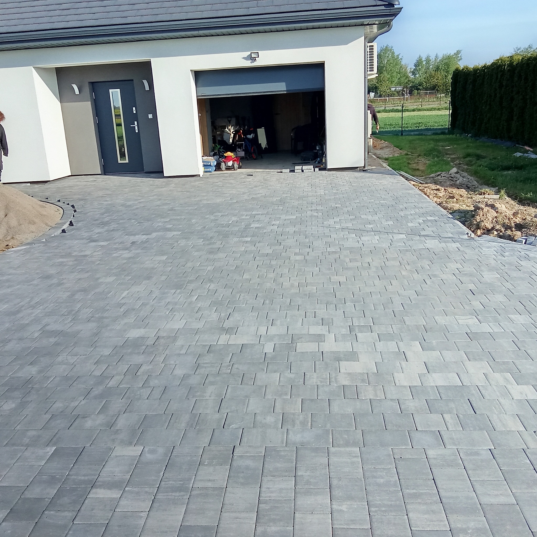 Nowoczesny podjazd z szarej kostki brukowej przy garażu w Bychawie. Widoczne przygotowania do dalszych prac ziemnych i wykończeniowych.