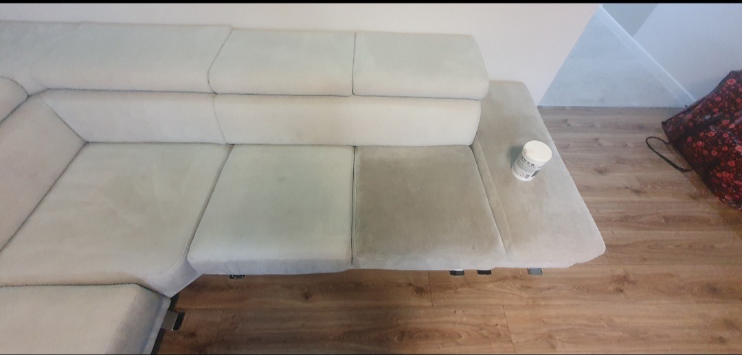 Fragment narożnika z widoczną różnicą w czystości między wypraną a niewypraną częścią, obok stoi pojemnik z preparatem czyszczącym.