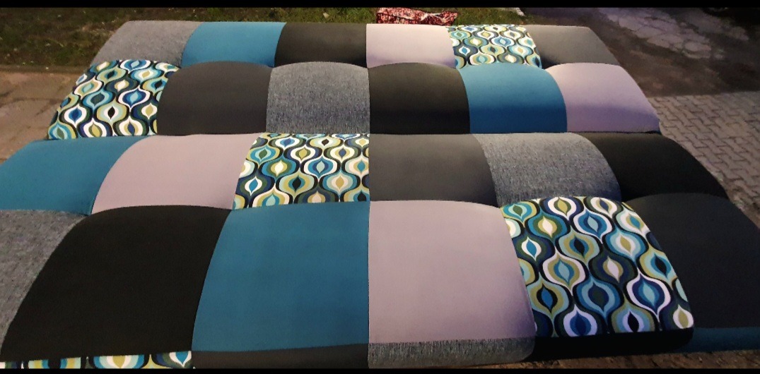 Wielobarwny materac z patchworku, z kwadratów w odcieniach szarości, błękitu, czerni i wzorzystej tkaniny w stylu retro, leżący na zewnątrz.