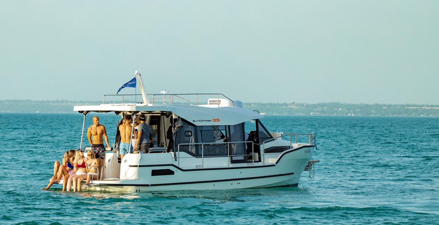 Grupa osób relaksuje się na pokładzie białego jachtu motorowego SunCamper 35 na wodach jeziora w okolicach Ostródy, widoczny mężczyzna bez koszulki.