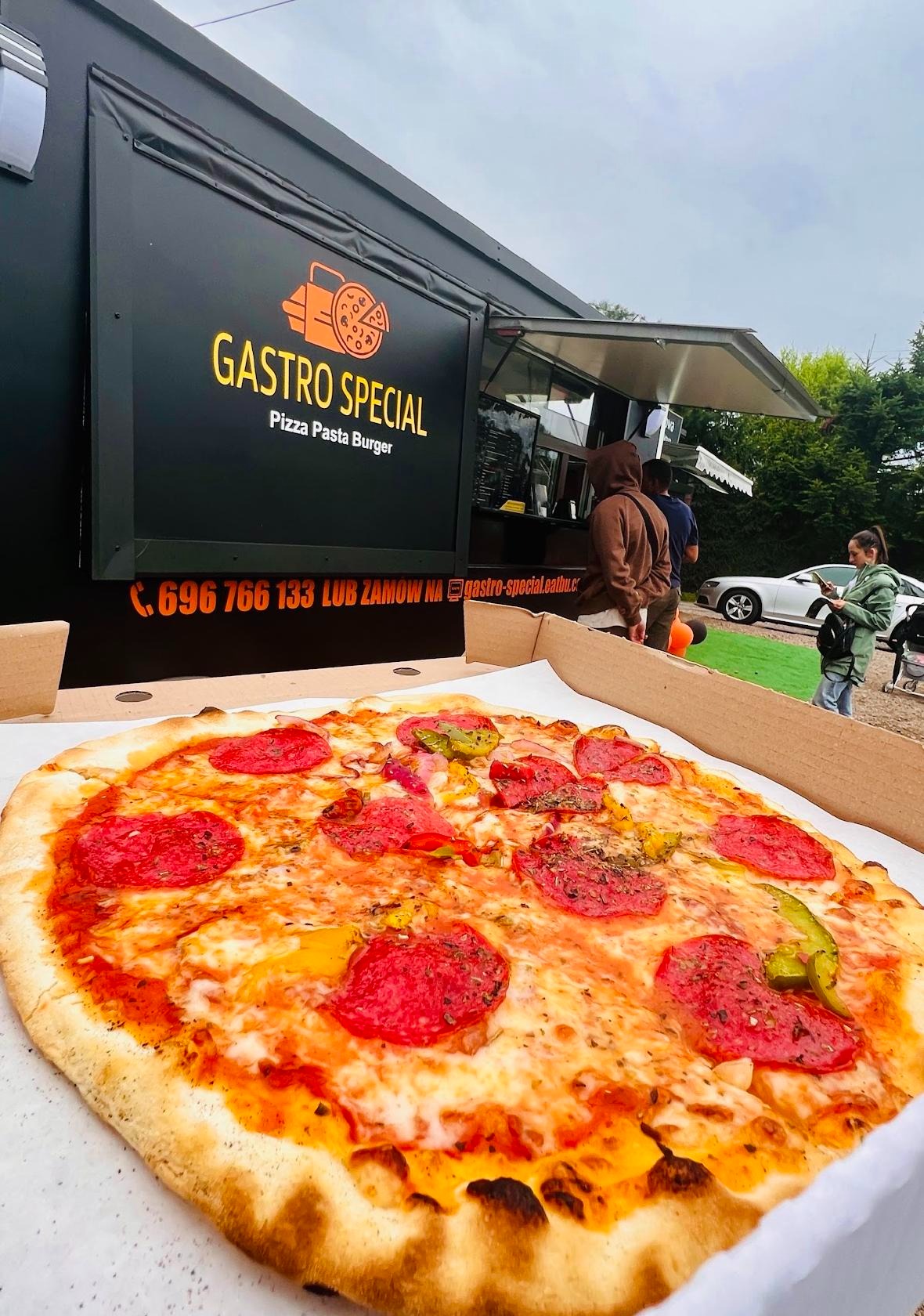 Pizza pepperoni w kartonie na tle food trucka Gastro Special z klientami w kolejce.