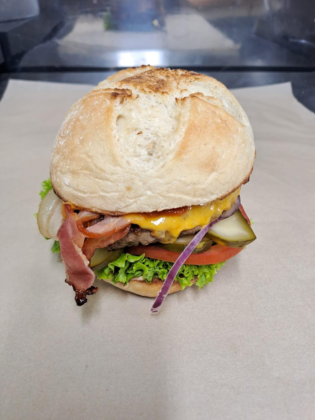 Apetyczny burger z wołowiną, serem cheddar, bekonem, pomidorem, ogórkiem kiszonym, czerwoną cebulą i sałatą, podany na papierze pergaminowym.