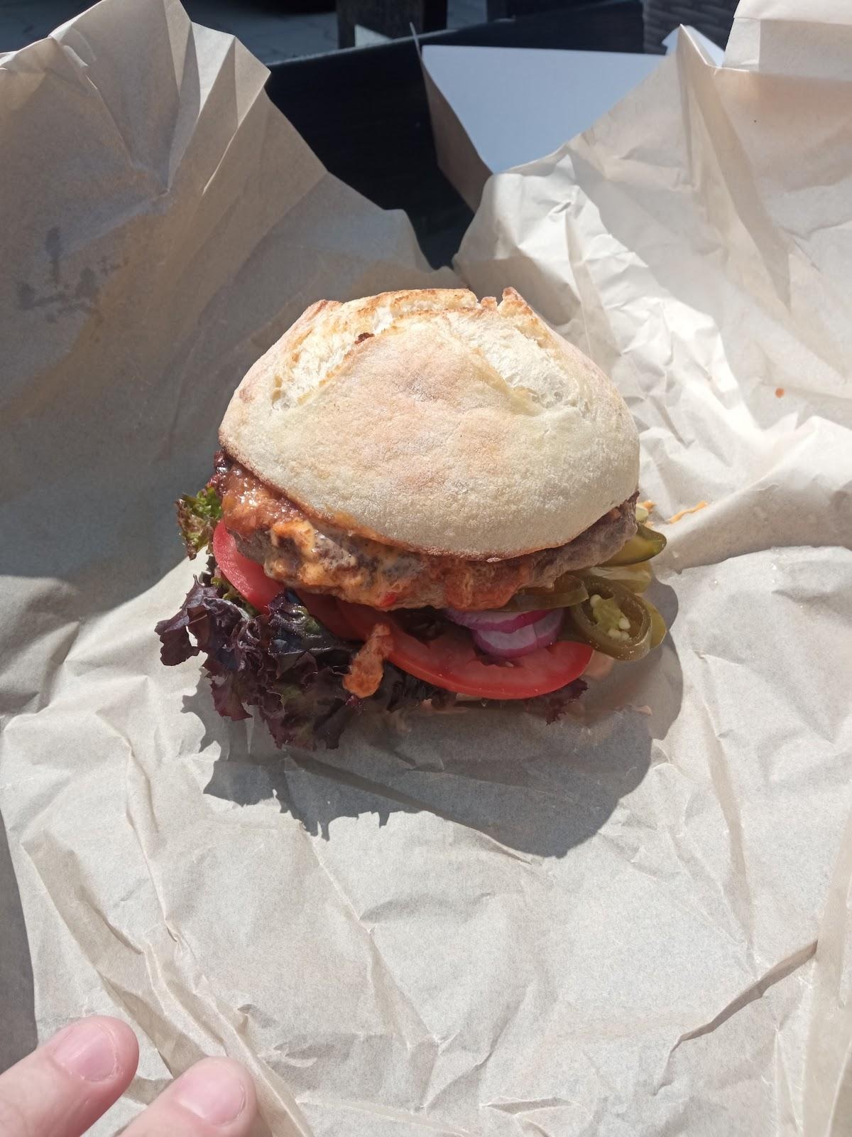 Apetyczny burger z wołowiną, sałatą, pomidorem, czerwoną cebulą i papryczkami jalapeno, podany na papierze do pakowania.