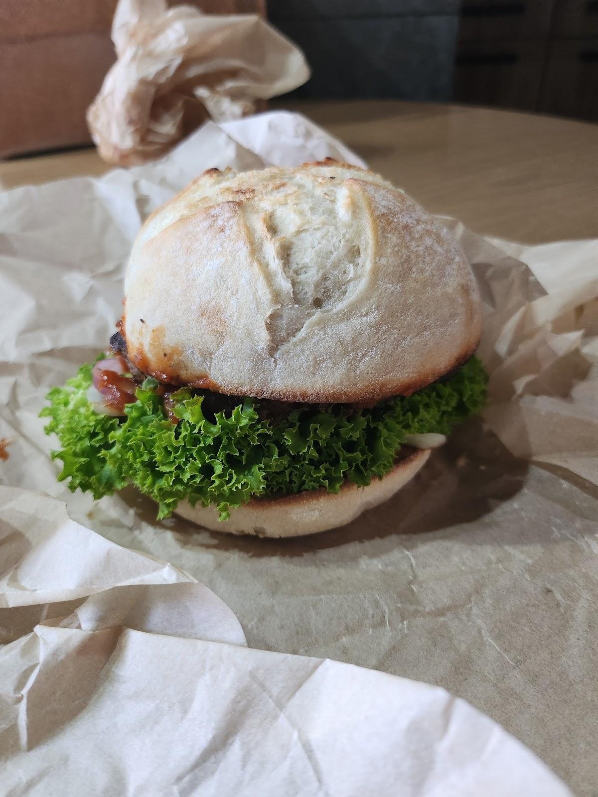 Burger z soczystą sałatą i sosem BBQ, podany na papierze pergaminowym.