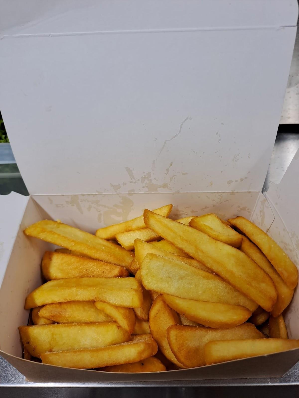 Porcja grubych frytek w białym kartonowym pudełku, widoczne ślady wilgoci na ściankach pudełka.