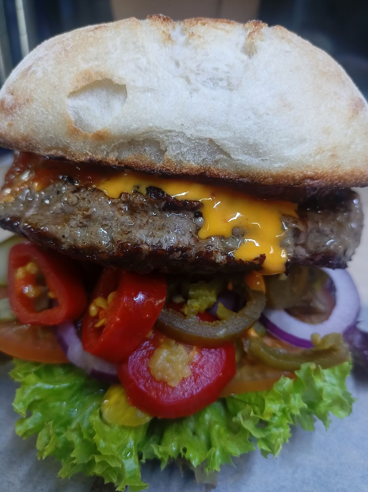 Soczysty burger z wołowiną, serem cheddar, świeżą sałatą, pomidorem, czerwoną cebulą i papryczkami jalapeno, podany w pszennej bułce.