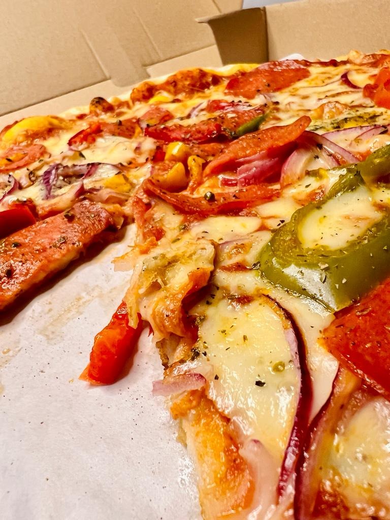 Pizza z pepperoni, papryką i czerwoną cebulą w kartonowym pudełku, widziana z bliska pod kątem.