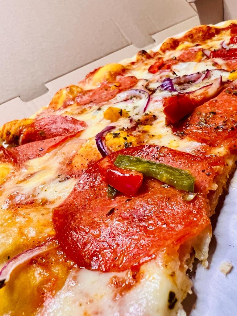 Kawałek pizzy pepperoni z czerwoną cebulą, papryką i ziołami w kartonowym pudełku, widok z bliska, z wyraźną fakturą składników.