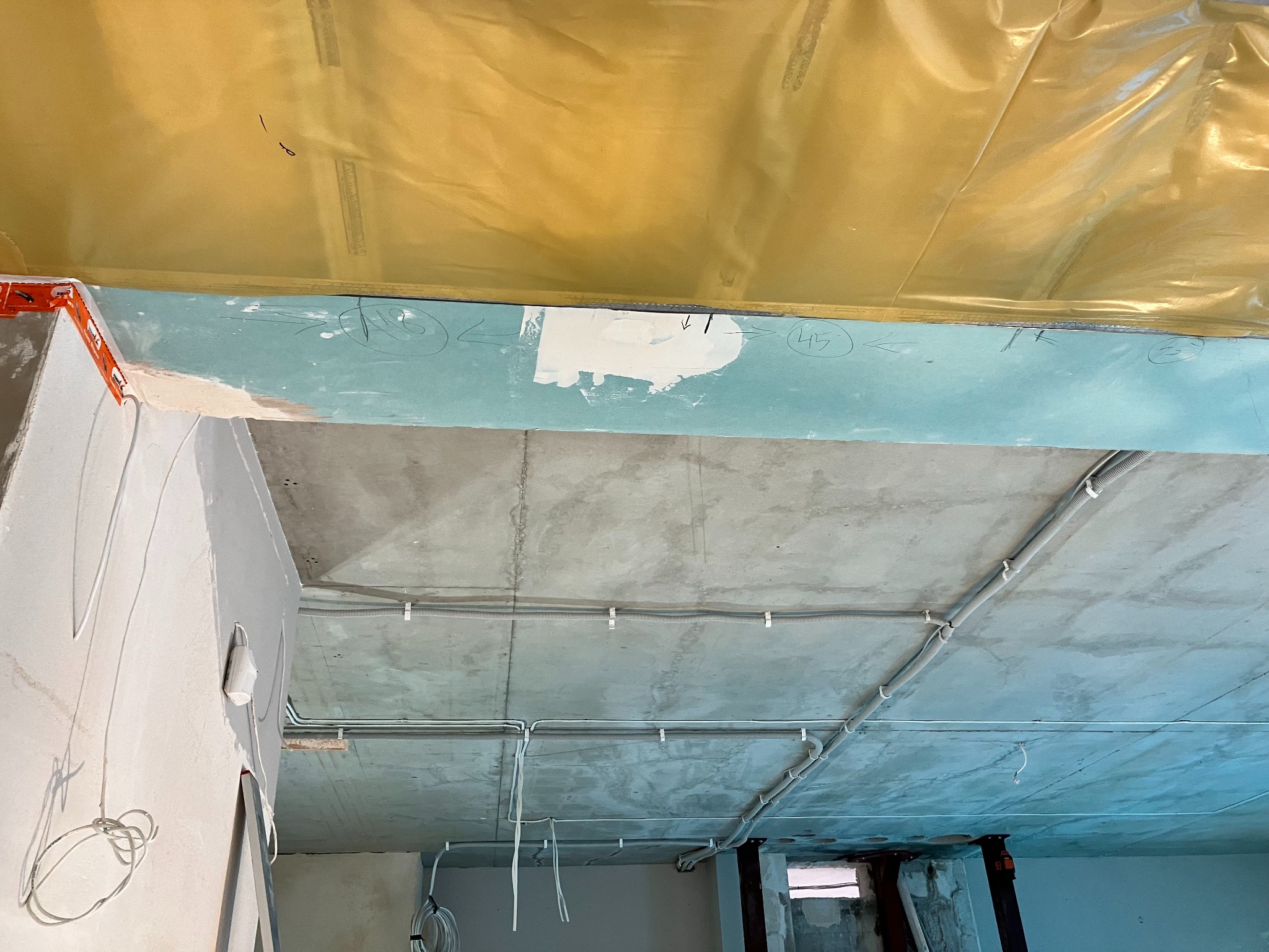 Sufit w trakcie remontu z widocznymi kablami w peszlach, fragmentem ściany z nałożoną gładzią i zabezpieczeniem folią malarską.