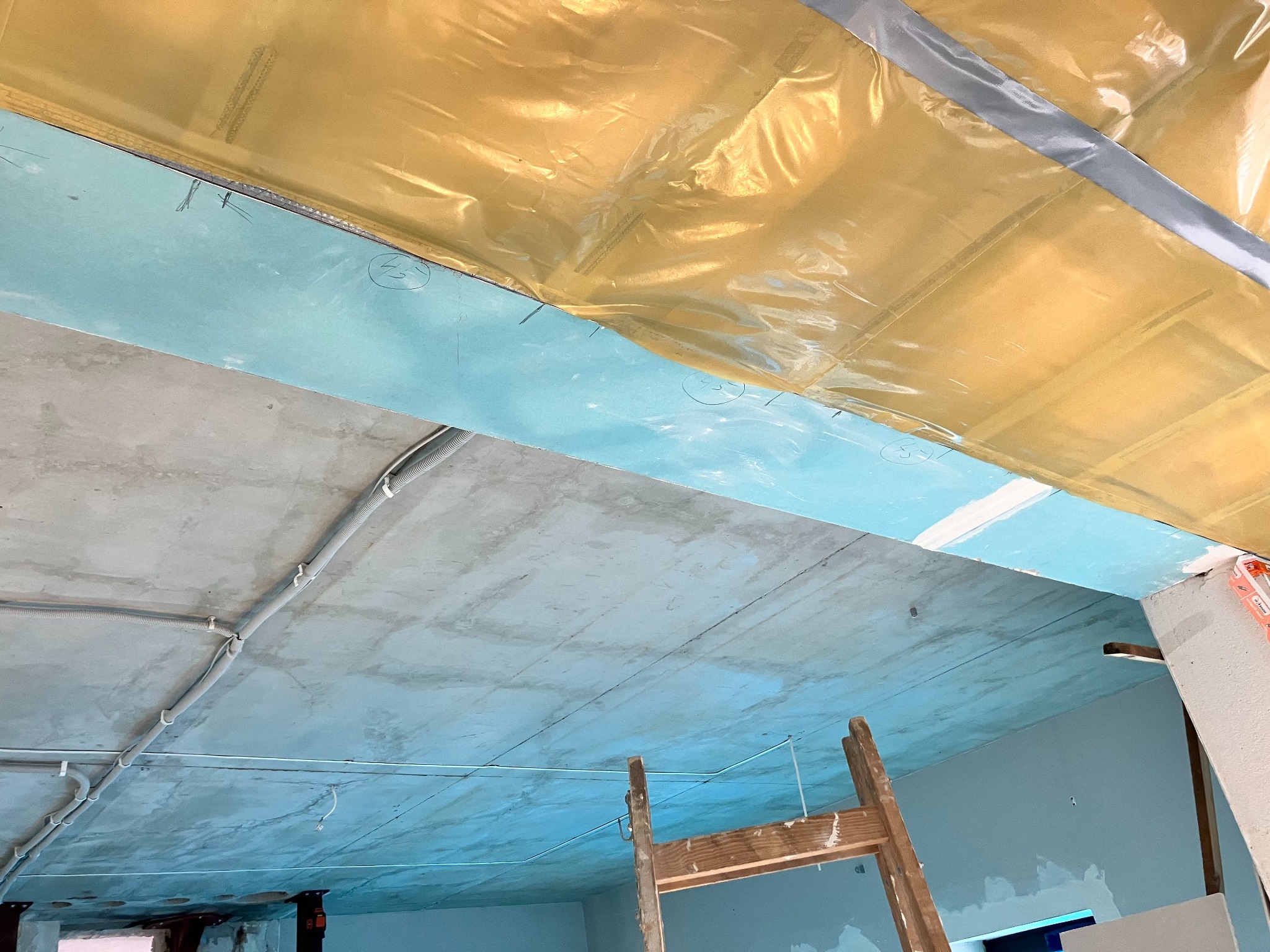 Montaż izolacji termicznej i folii paroizolacyjnej na suficie podwieszanym, widoczne kable elektryczne i drabina drewniana.