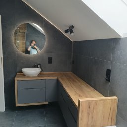 Perfect wykończenia wnętrz Damian Oszczęda - Nowoczesna łazienka na poddaszu z szarą glazurą, okrągłym lustrem z podświetleniem LED i drewnianym blatem szafki umywalkowej. Widoczna osoba robiąca zdjęcie w lustrze.