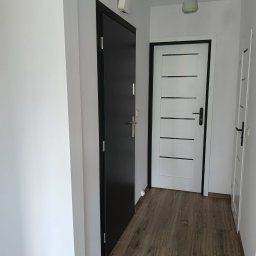 Perfect wykończenia wnętrz Damian Oszczęda - Nowoczesny przedpokój z dwiema parami drzwi: czarne drzwi wejściowe i białe drzwi wewnętrzne z czarnymi akcentami, oświetlone wiszącą lampą.