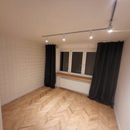 Perfect wykończenia wnętrz Damian Oszczęda - Pokój po remoncie: parkiet w jodełkę, okno z parapetem, grzejnik, szyny z oświetleniem punktowym i zasłony. Ściany z delikatnym wzorem. Widok na wnętrze.