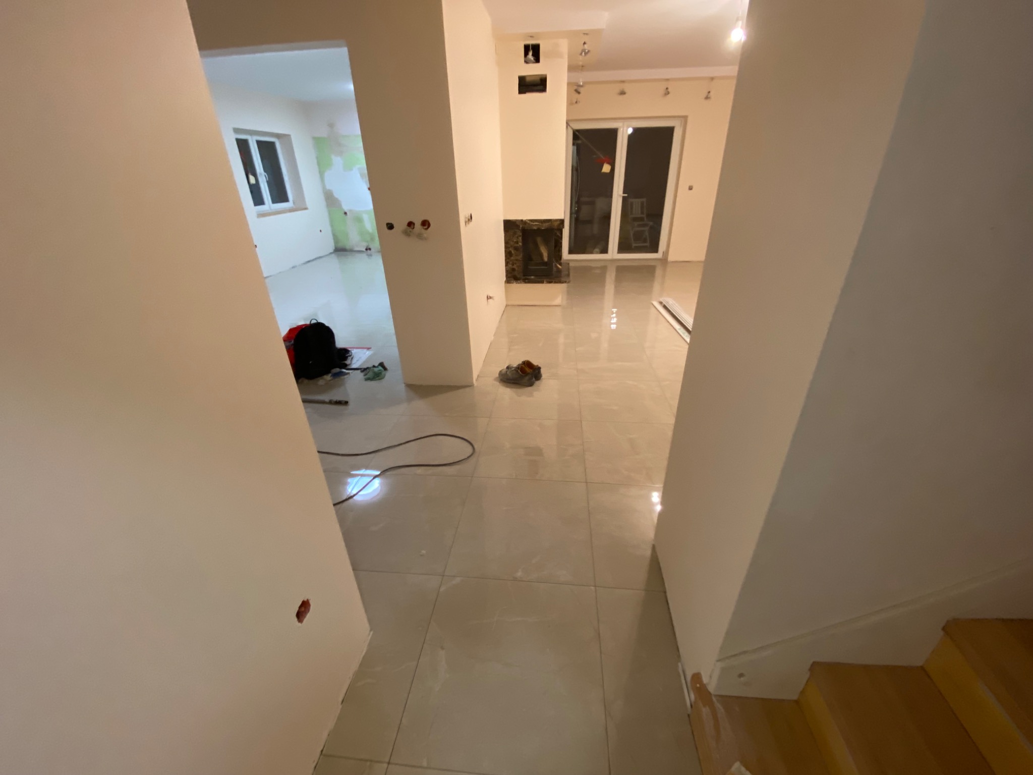 Wnętrze w trakcie wykańczania: świeżo położone płytki podłogowe, gładkie ściany, widoczne przygotowania do montażu gniazdek elektrycznych i fragment schodów.