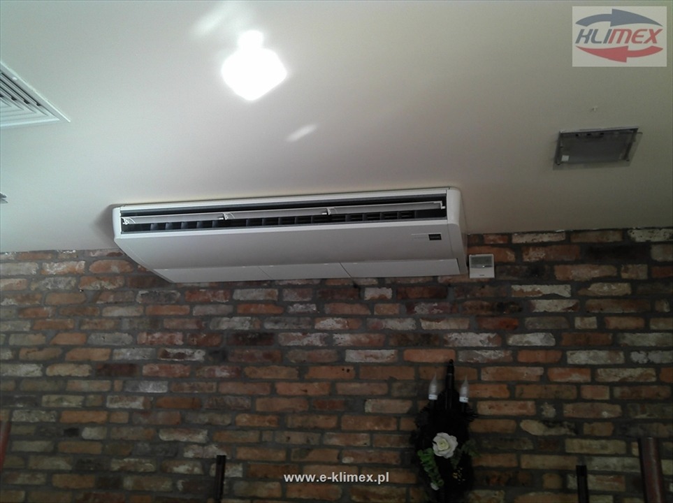 Zamontowany klimatyzator kasetonowy na ceglanej ścianie w Lipkach Wielkich, widoczny także panel sterowania i kratka wentylacyjna w suficie.