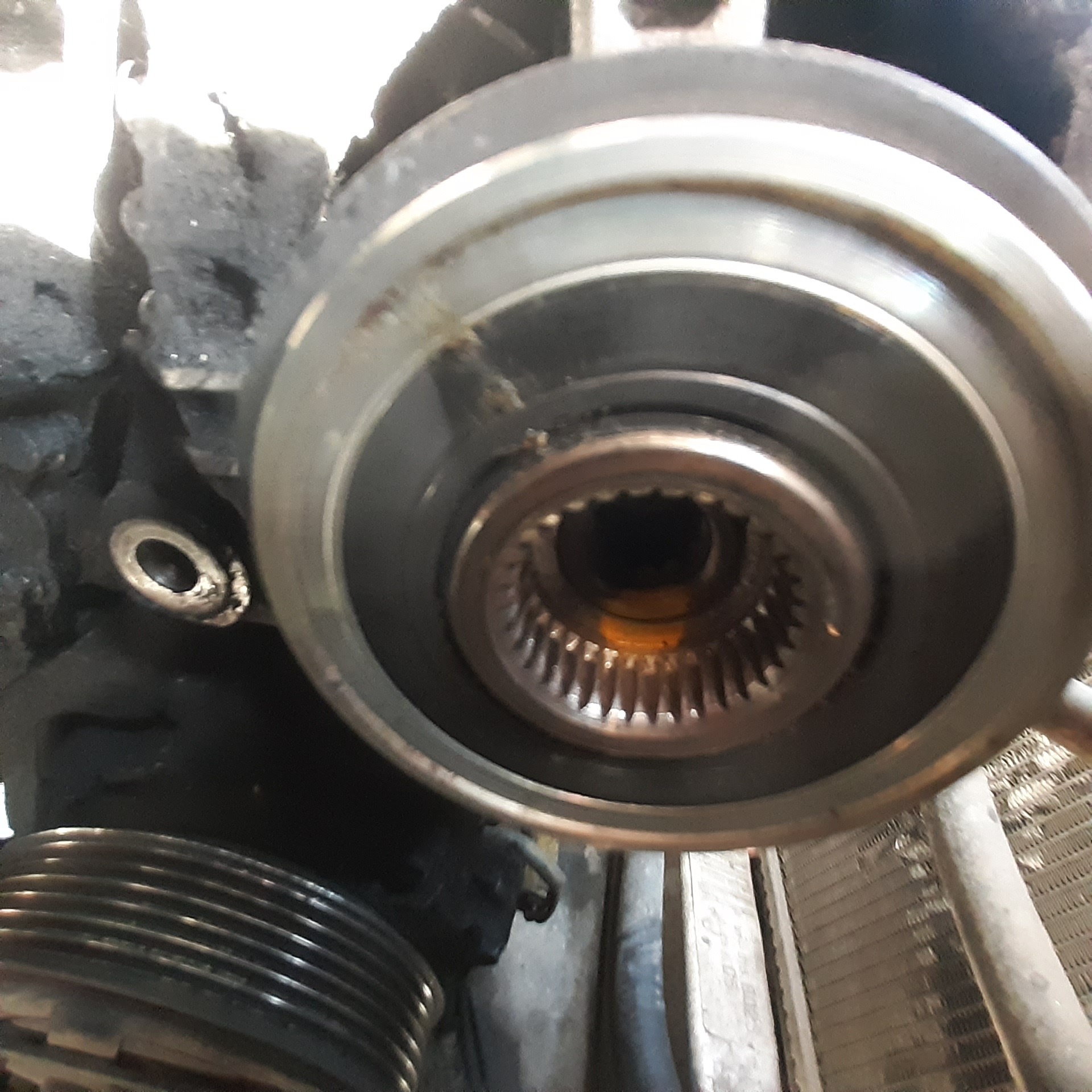 Detail of a car engine component showing a splined shaft and pulley system, with visible wear and grease accumulation, suggesting maintenance or repair work.