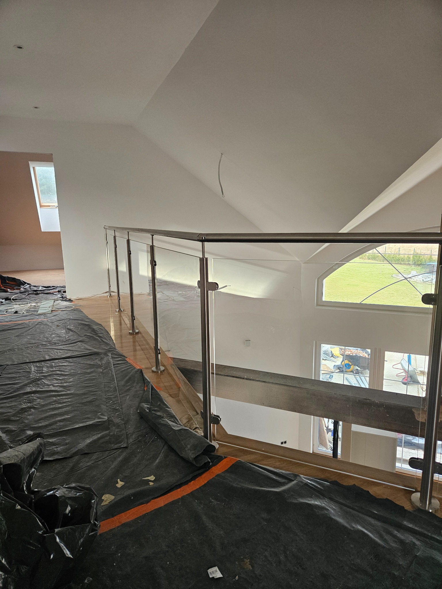 Wnętrze domu w trakcie wykańczania, widok na szklaną balustradę z metalowymi słupkami, podłoga zabezpieczona folią ochronną.
