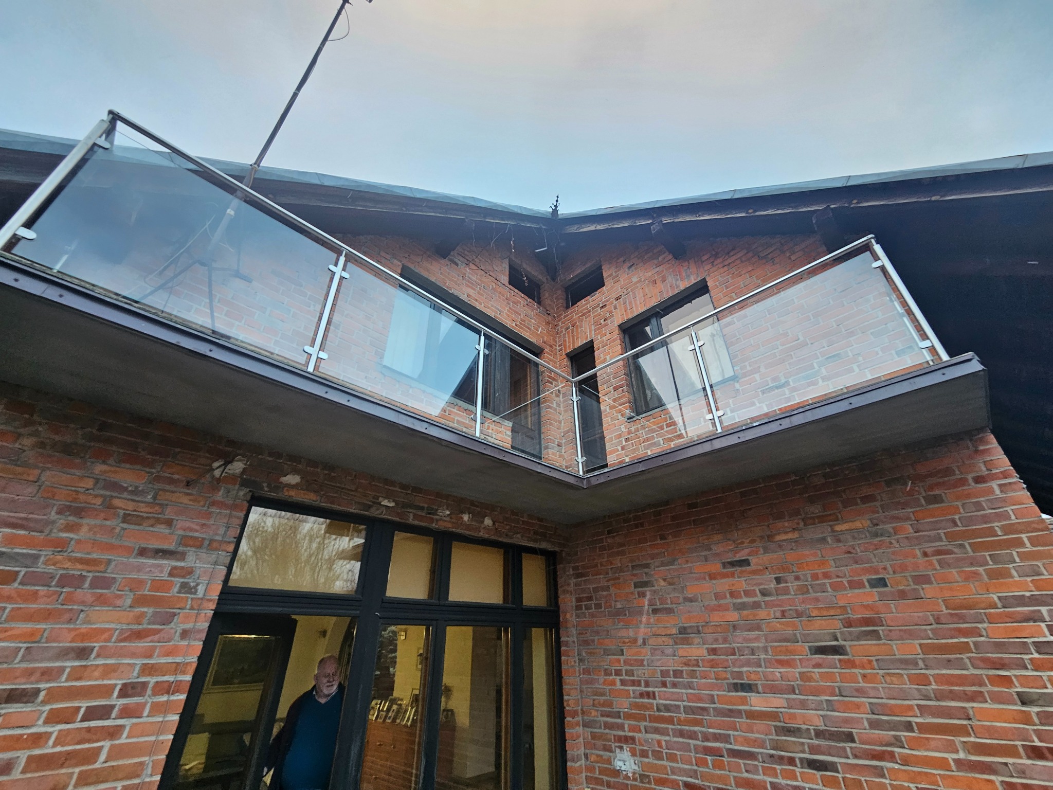 Dwupoziomowy balkon z przezroczystymi panelami na tle ceglanej elewacji budynku, widok z dołu.