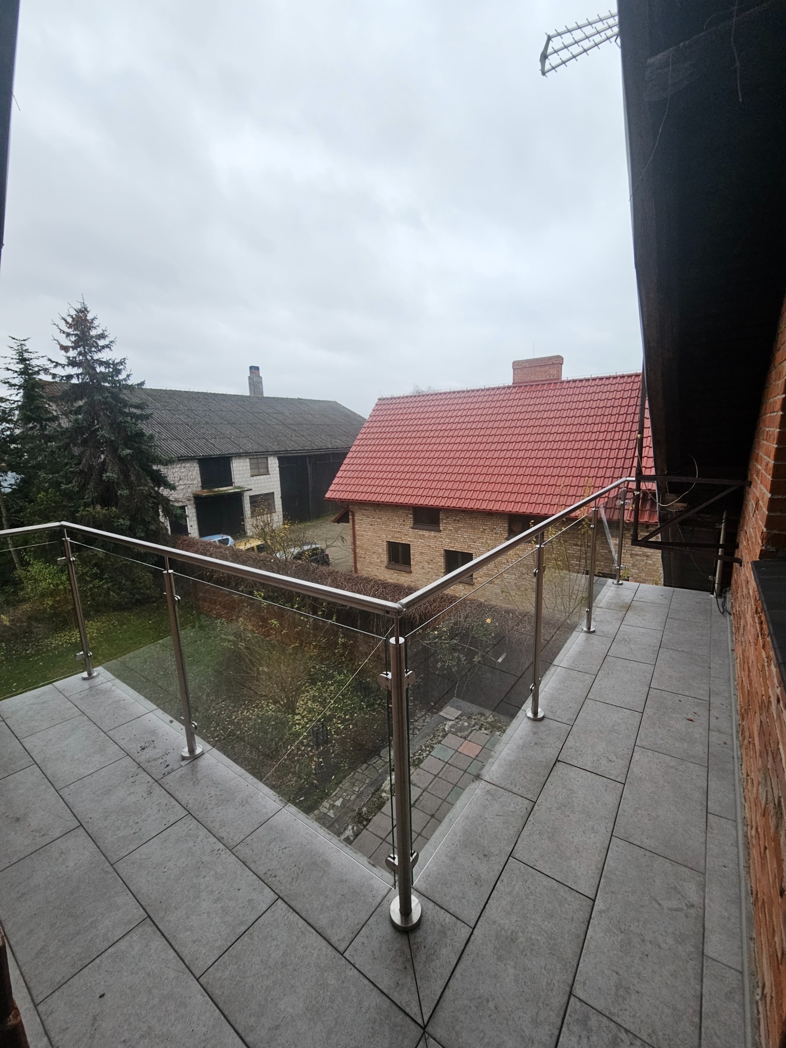Szklana balustrada na balkonie z widokiem na budynki mieszkalne w pochmurny dzień.