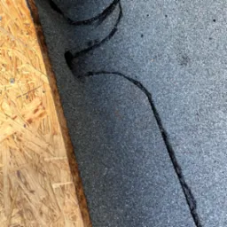 Fragment dachu pokrytego papą z widocznymi śladami uszczelniania pęknięć czarną masą bitumiczną, obok płyta OSB.