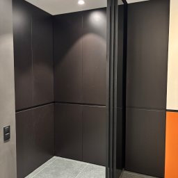 Iryna Zhabenko - Nowoczesna szafa wnękowa z przesuwnymi drzwiami w ciemnym kolorze, szare płytki podłogowe, minimalistyczny design, widoczne detale wykończenia.