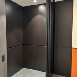 Nowoczesna szafa wnękowa z przesuwnymi drzwiami w ciemnym kolorze, szare płytki podłogowe, minimalistyczny design, widoczne detale wykończenia.