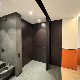 Iryna Zhabenko - Nowoczesna łazienka z bidetem, szarą płytką i czarnymi elementami: ściany, drzwi przesuwne. Kontrastujące pomarańczowe i białe akcenty na ścianie.