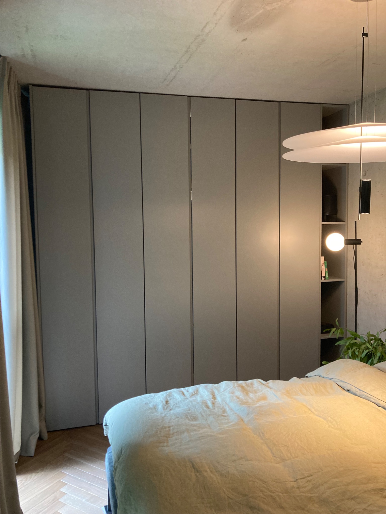 Szafa wnękowa w kolorze szarym, zintegrowana z regałem, widoczna w sypialni z łóżkiem i lampą wiszącą.