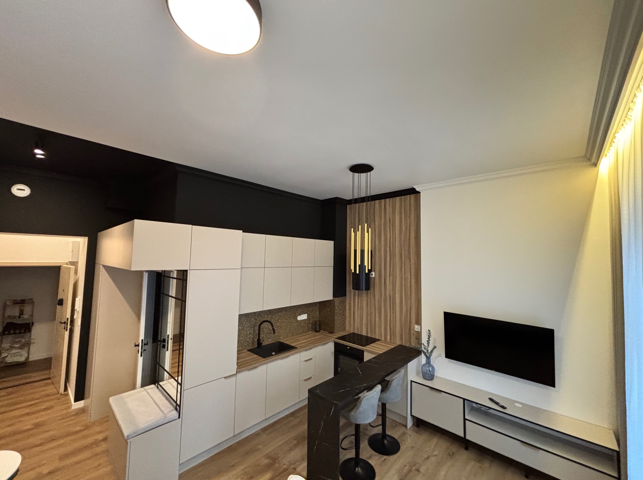 Nowoczesna kuchnia z barkiem i oświetleniem punktowym, widok z góry, beżowe fronty szafek, czarny blat i elementy dekoracyjne, drewniana podłoga.