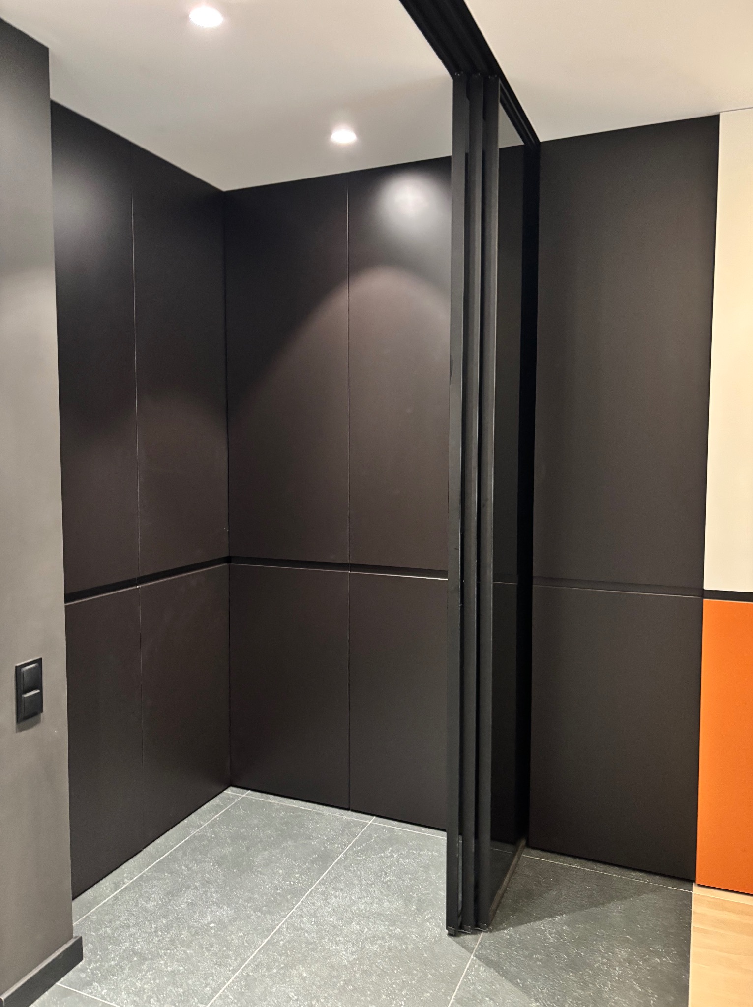 Nowoczesna szafa wnękowa z przesuwnymi drzwiami w ciemnym kolorze, szare płytki podłogowe, minimalistyczny design, widoczne detale wykończenia.