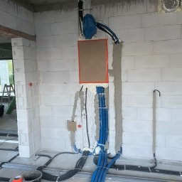 AROS Adam Rosiek - Wewnętrzne rozprowadzenie instalacji elektrycznej w budynku w trakcie budowy. Widoczne kable w peszlach, puszki instalacyjne i pianka montażowa.