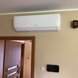 KWADRAT MB ŻABKIEWICZ ANETA - Biały klimatyzator marki AUX zamontowany na beżowej ścianie w domu, obok czarny głośnik i wideodomofon.