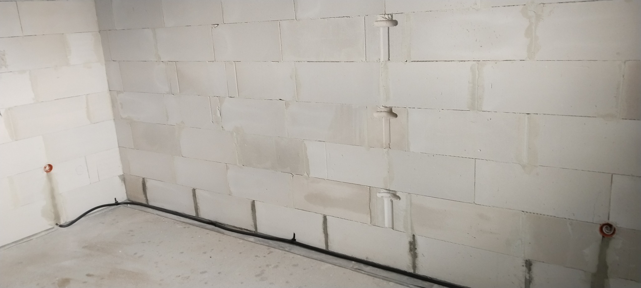 Surowy stan ścian z betonu komórkowego wewnątrz budynku, z widocznymi puszkami elektrycznymi i przewodami biegnącymi po podłodze.