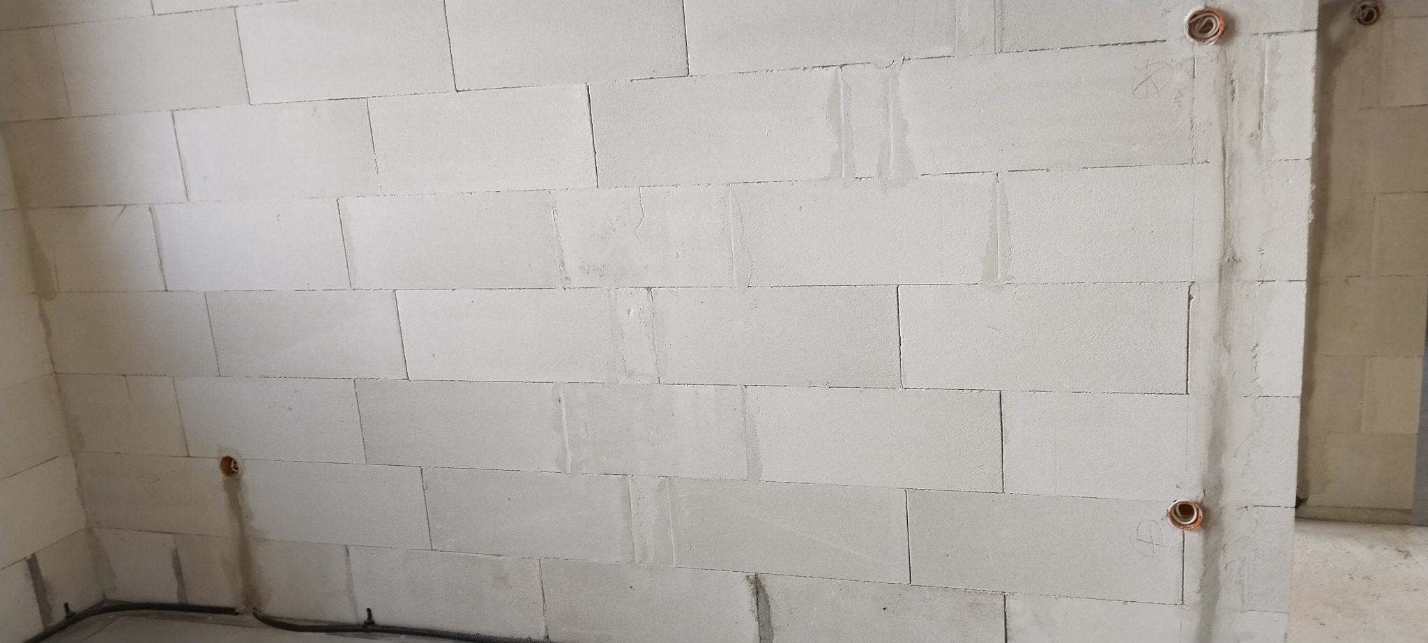 Murowana ściana z betonu komórkowego z widocznymi puszkami instalacyjnymi i przewodami elektrycznymi u dołu.