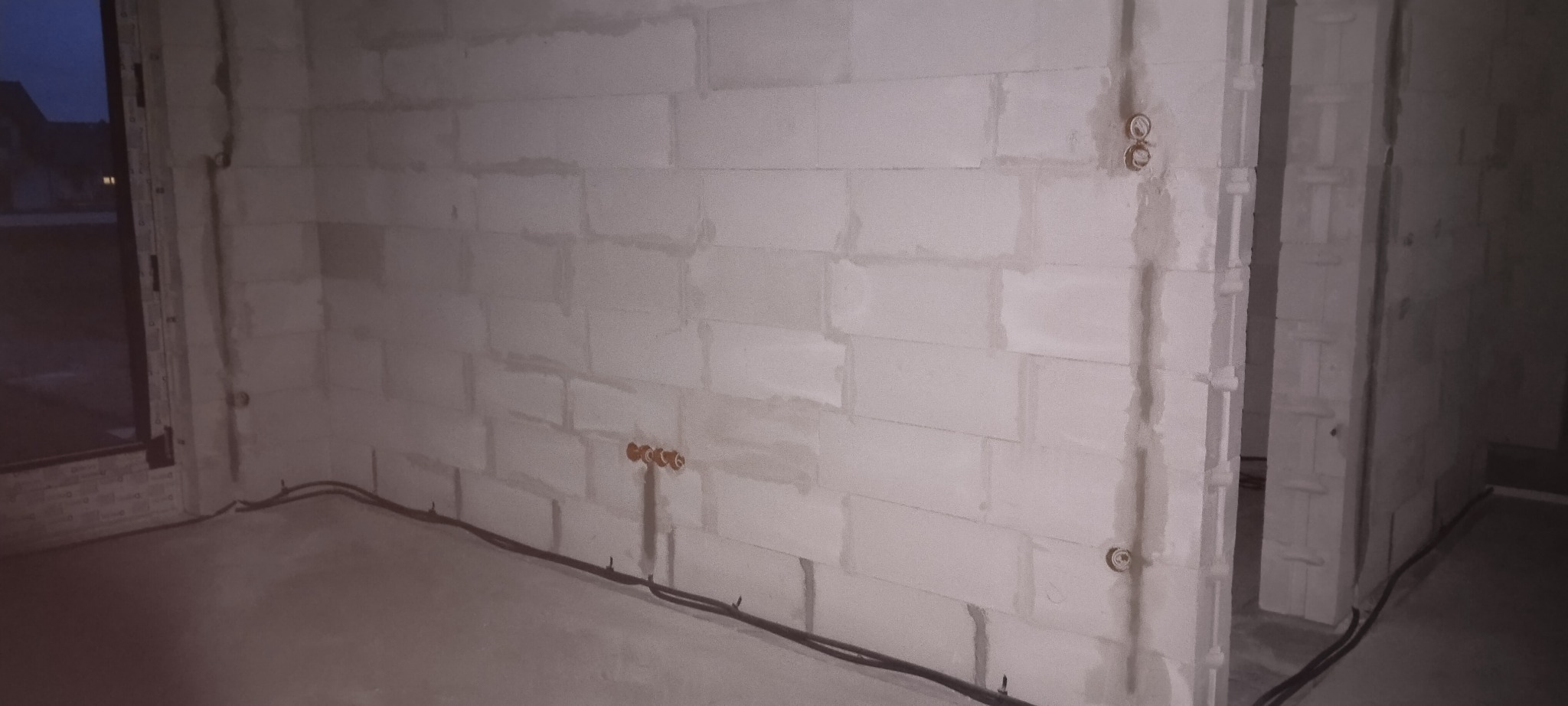 Surowy stan wnętrza z widocznymi przewodami elektrycznymi poprowadzonymi wzdłuż ściany z betonu komórkowego i puszkami instalacyjnymi w ścianie.