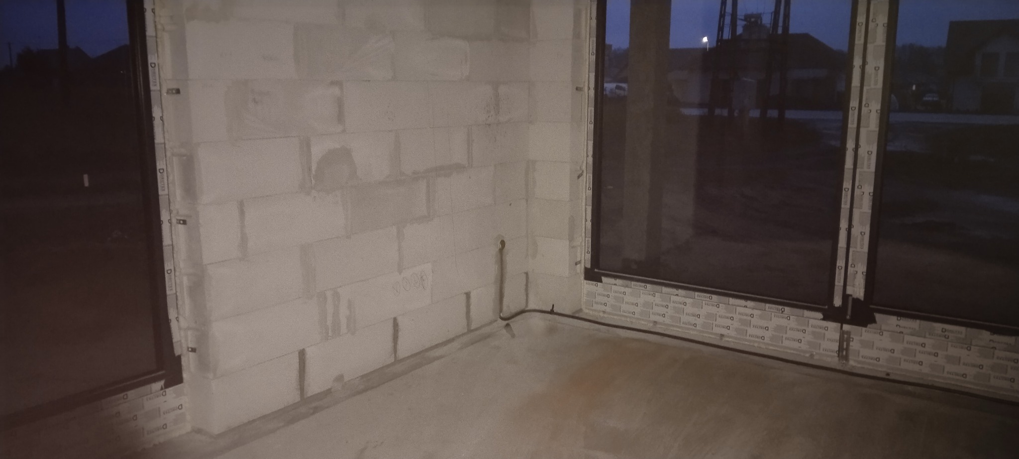 Surowy stan wnętrza budynku w Łabiszynie, z widocznymi oknami i ścianami z bloczków betonowych, przygotowane pod instalacje elektryczne, z przewodami wystającymi ze ściany.