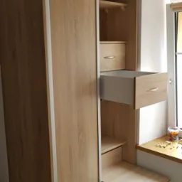 Jasna szafa wnękowa z przesuwnymi drzwiami i wysuwanymi elementami w Jeleniej Górze, widok na otwartą szufladę i wysuwany blat roboczy.