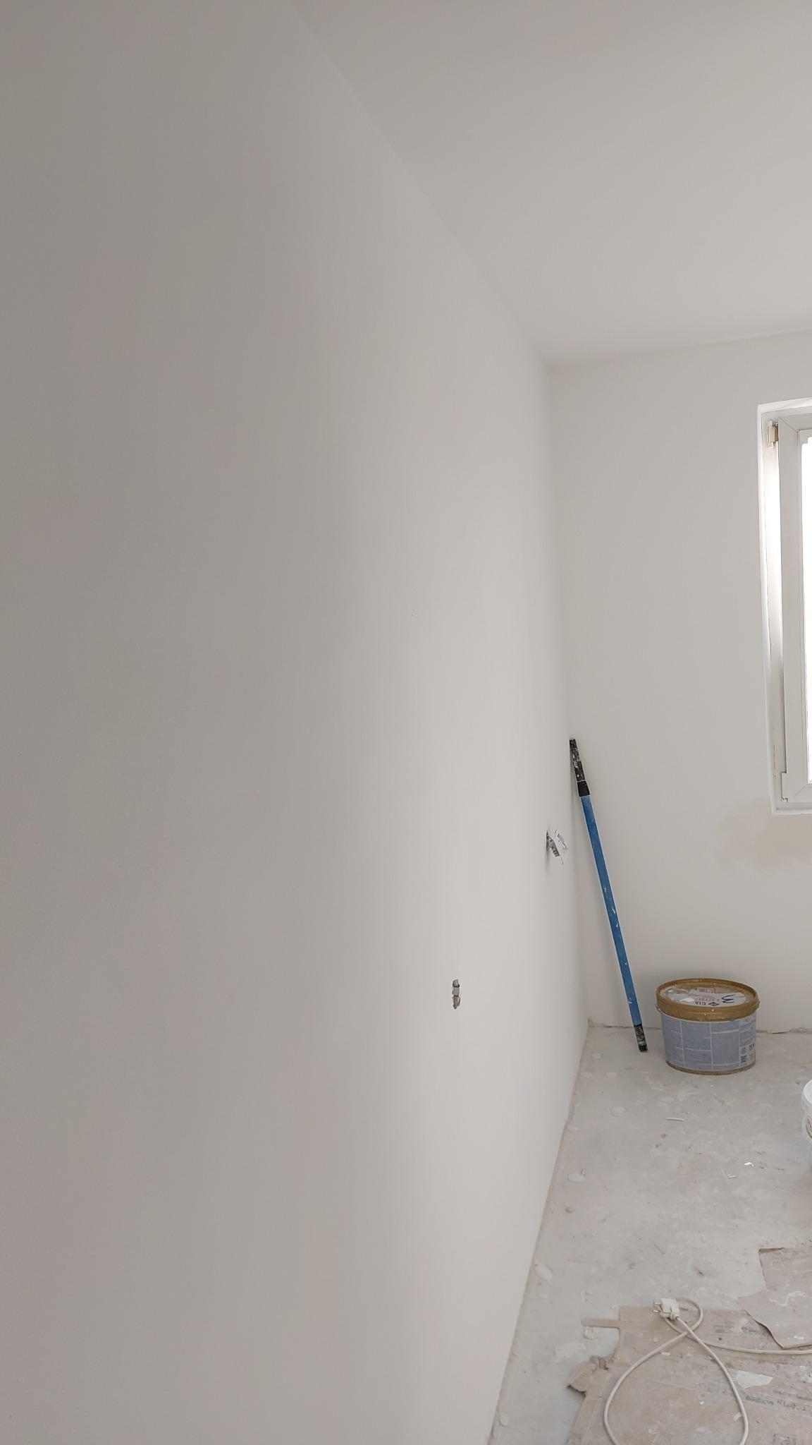 Świeżo pomalowane na biało wnętrze pokoju z widoczną puszką farby, wałkiem opartym o ścianę i wystającymi przewodami elektrycznymi