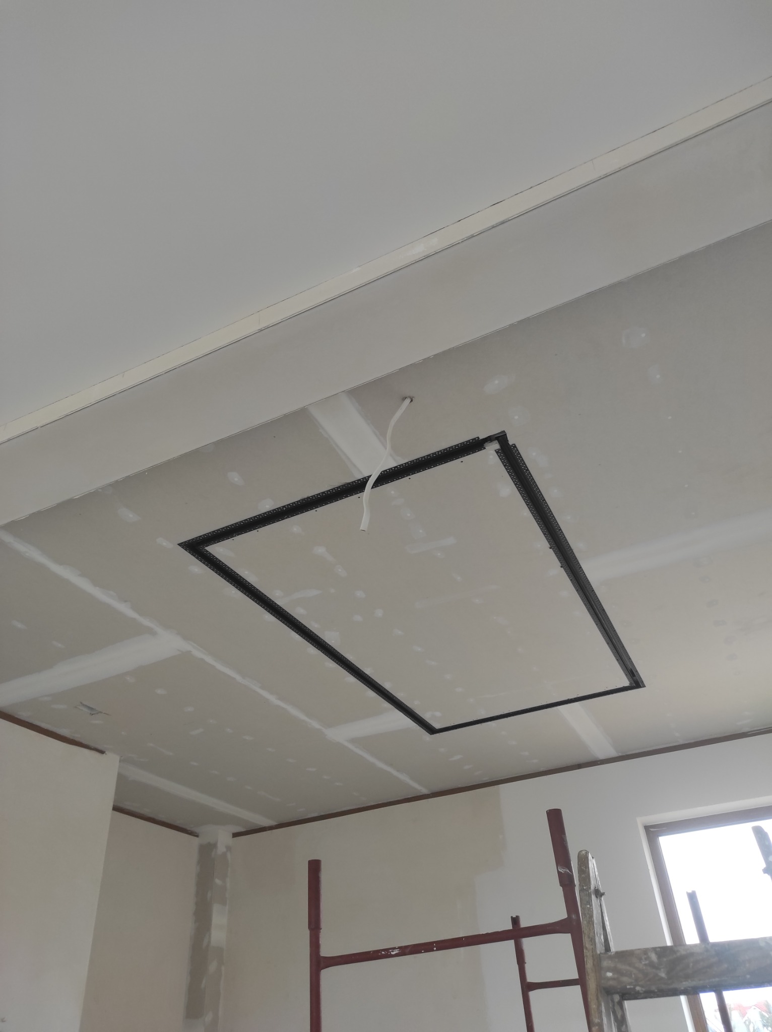 Sufit z zamontowaną klapą rewizyjną, widoczne łączenia płyt, szpachlowane, surowy kabel zwisający z otworu.