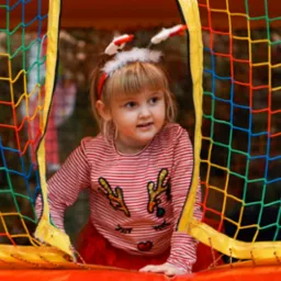 Dziewczynka w stroju świątecznym wychodzi z dmuchanego, kolorowego placu zabaw z siatką ochronną.