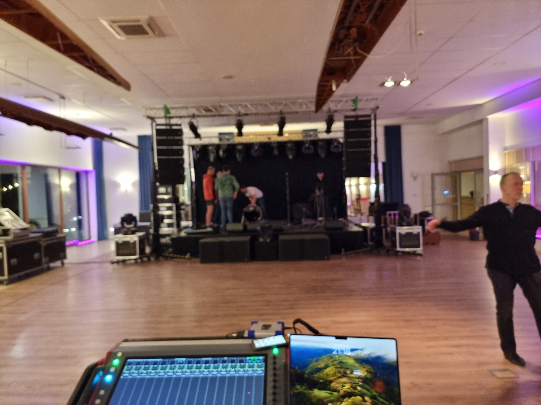 Przygotowania do wydarzenia: ekipa techniczna ustawia nagłośnienie i oświetlenie na scenie, widoczny mikser dźwięku i laptop z tapetą górską.