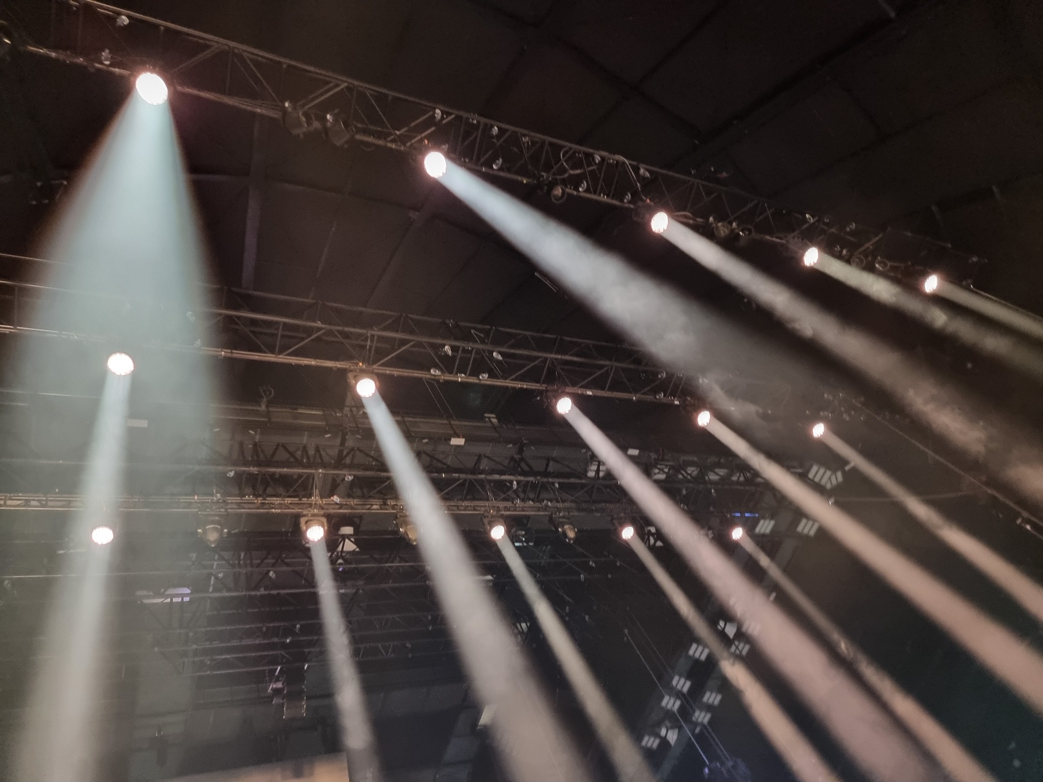 Scena z widocznym systemem oświetleniowym: reflektory punktowe skierowane w dół, tworzące smugi światła w przestrzeni.