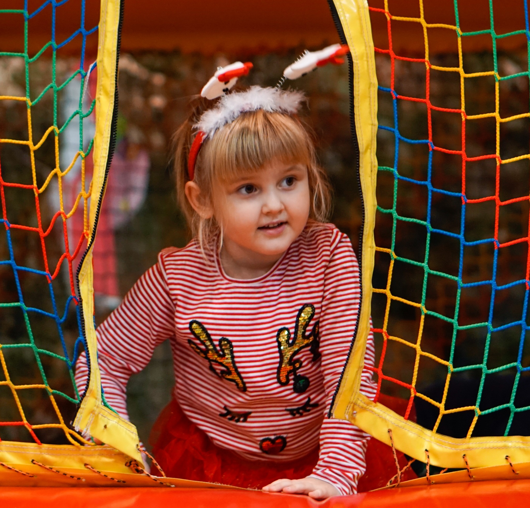 Dziewczynka w stroju świątecznym wychodzi z dmuchanego, kolorowego placu zabaw z siatką ochronną.