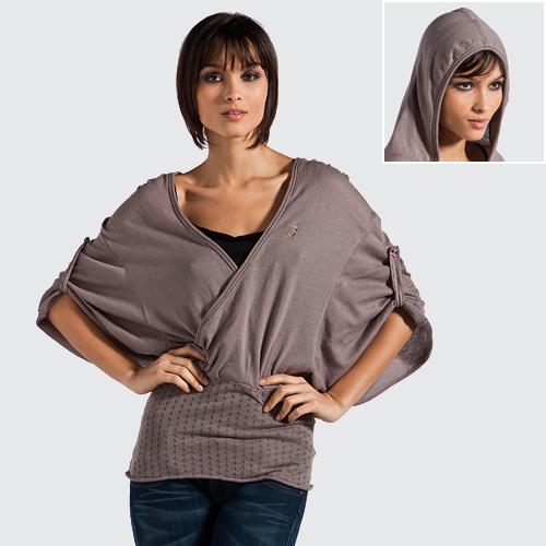 Kobieta prezentuje bluzkę w stylu kimono z szerokimi rękawami i kapturem w tle, część kolekcji outlet stock odzieży markowej.